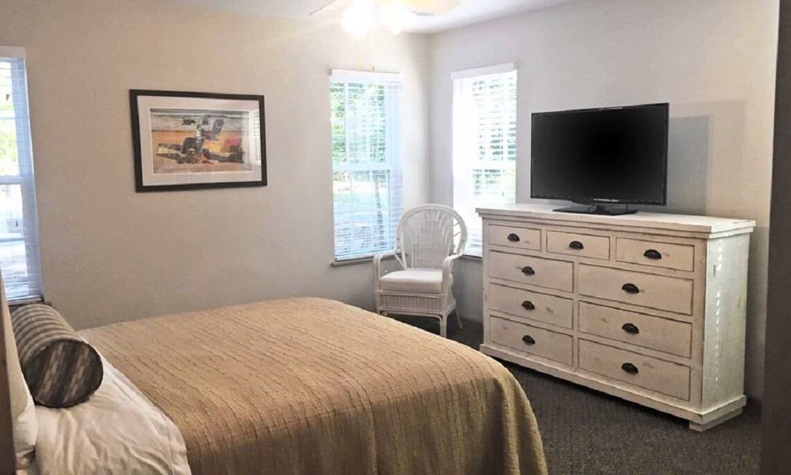 Un dormitorio con cama, cómoda, televisor y silla.