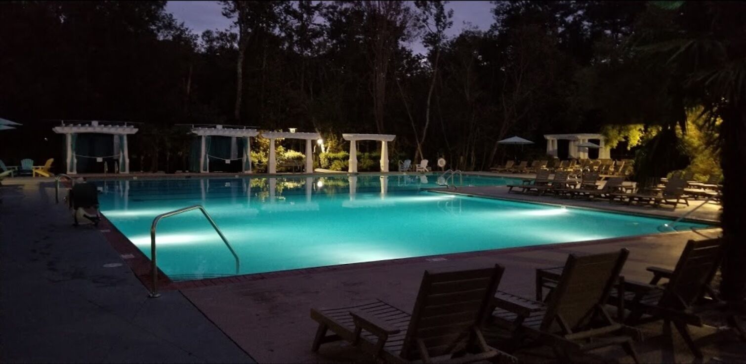 A swimming pool with lounge chairs and umbrellas, surrounded by trees.