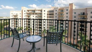 A balcony with two chairs and a table, overlooking a residential building complex. - Pompano Beach | Family Golf Vacation | Pool + Golf | 2BR (Pompano Beach)