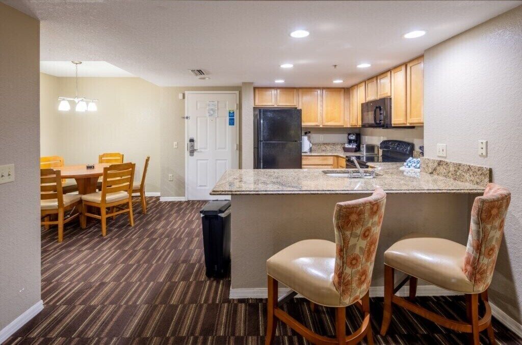Una cocina compacta con una isla central, armarios de madera y un comedor con sillas.