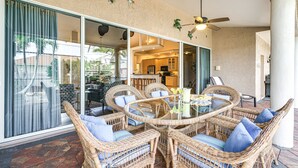 An outdoor dining area with wicker furniture and a glass table, connected to a kitchen and living space through large sliding glass doors. - Spacious Oasis w/ Lagoon Pool & Spa in Cape Coral! (Cape Coral)