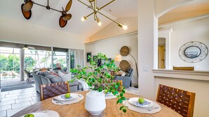 A dining area with a wooden table set for four, a white vase with green plants, and a view of the outdoors through large windows. - Spacious Oasis w/ Lagoon Pool & Spa in Cape Coral! (Cape Coral)