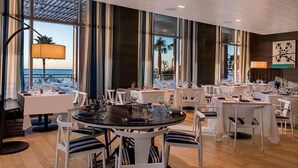 A restaurant with multiple tables, large windows, and a view of the ocean.