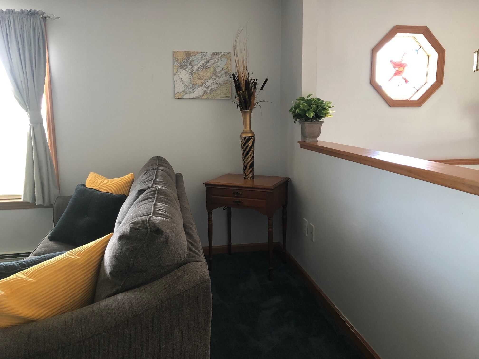 Uma sala de estar com sofá, mesa de madeira, vaso, quadro emoldurado e janela com cortinas.