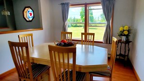 Un comedor con una mesa redonda, cuatro sillas de madera, una cesta de frutas y una ventana con cortinas.