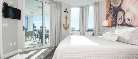 A hotel room with a large bed, a ceiling fan, a television, and a view of the city through the sliding glass doors.