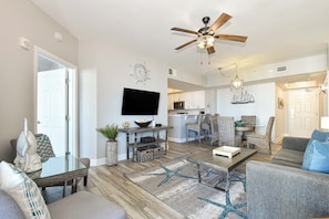 A spacious living room with a flat-screen TV, a ceiling fan, and a dining area with wicker furniture. - 2-bedroom resort condo w/private balcony & lagoon pool! 🌴 (Destin)