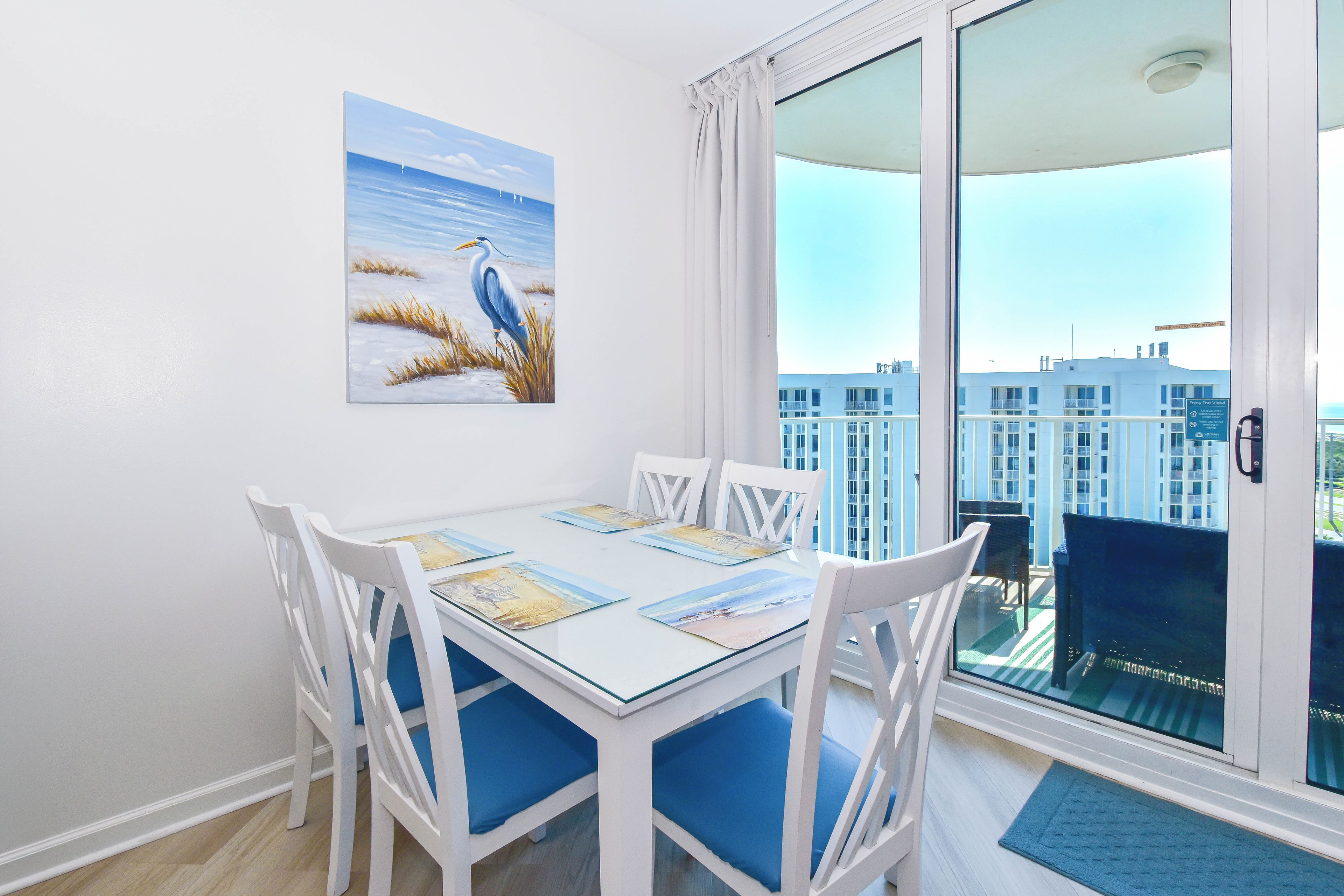 Un comedor con una mesa lista para cuatro, sillas blancas y vistas de la ciudad a través de un gran ventanal.