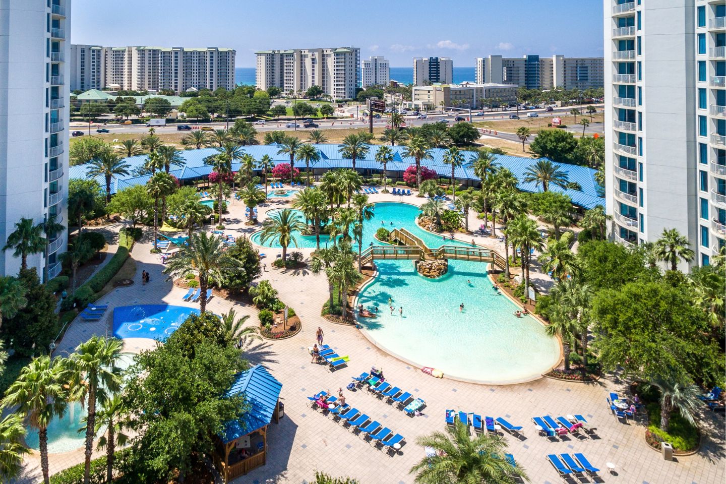 A resort with multiple swimming pools, palm trees, and a beach area with sun loungers.