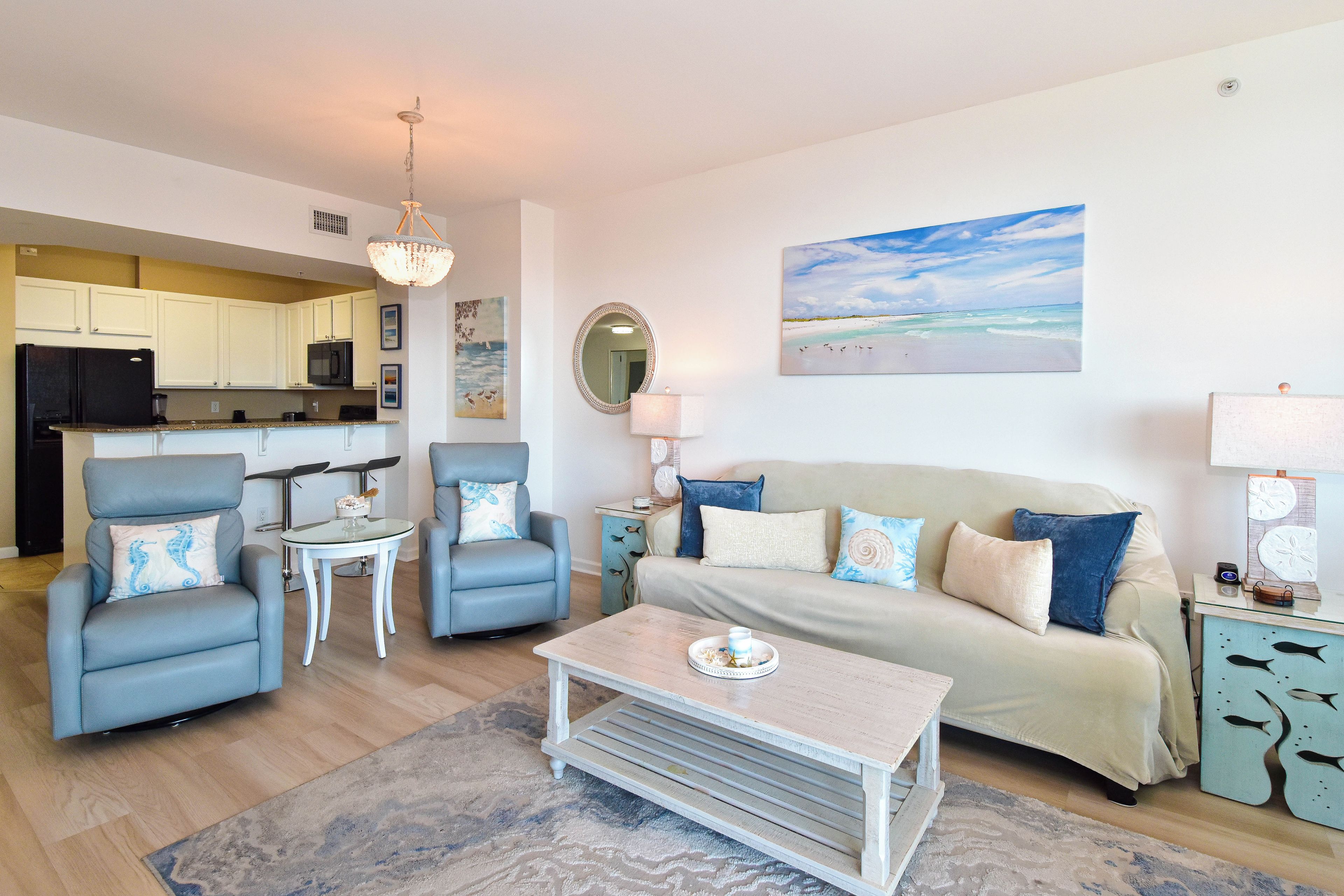 A living room with a sofa, two armchairs, a coffee table, and a kitchen in the background.