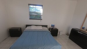 A bedroom with a bed, two nightstands, a dresser, a window with blinds, and a mirror.