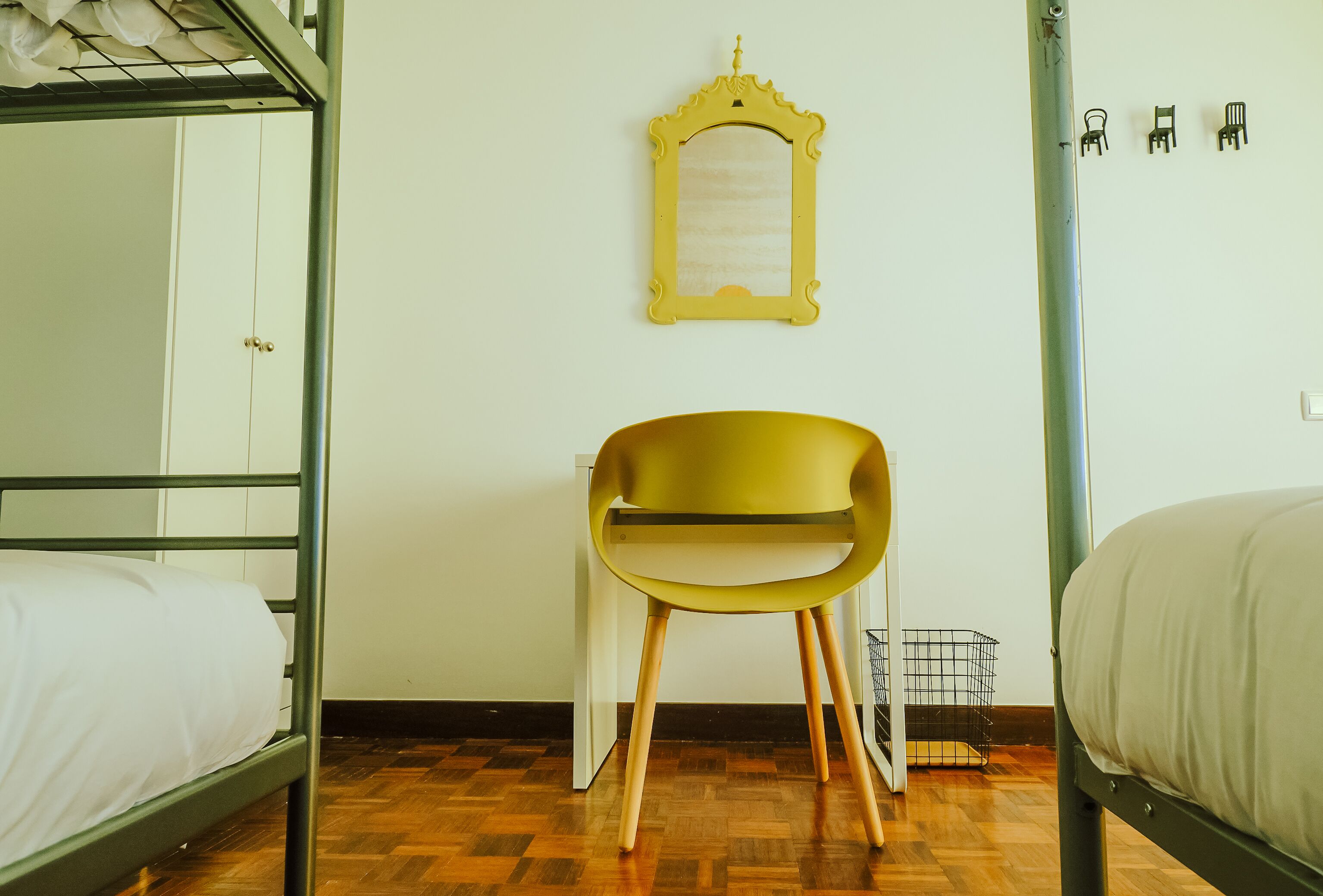 Un dormitorio con literas, una silla amarilla, un espejo y un perchero de metal.