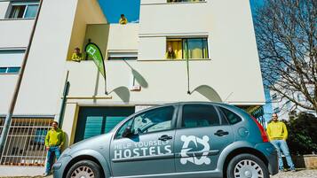A car with "HELP YOURSELF HOSTELS" branding parked in front of a building with multiple windows and balconies.