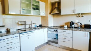 A modern kitchen with white cabinets, a dishwasher, an oven, and a coffee maker. - Help Yourself Hostels - Restelo (Lisbon)
