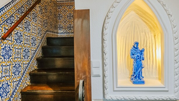 A staircase with ornate blue and white tiles, a wooden handrail, and a statue in a niche. - Help Yourself Hostels - Restelo (Lisbon)