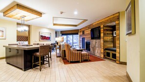 A modern kitchen with a central island, bar stools, a dining area with a high chair, and a fireplace.