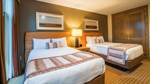 A hotel room with two beds, a wooden headboard, a nightstand with a lamp, and a large wardrobe.