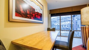 A conference room with a wooden table, chairs, a large abstract painting, and a view of a snowy cityscape through large windows. - Avon Colorado | Friends Ski Retreat | Hot Tub + Ski | 2BR (Avon)