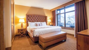 A hotel room with a large bed, a wooden headboard, two bedside lamps, a window with curtains, and a view of a building outside. - Avon Colorado | Friends Ski Retreat | Hot Tub + Ski | 2BR (Avon)