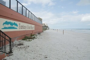 A beachside view of Fantasy Island Resort II with a signboard, sandy beach, and ocean in the background. - Daytona Beach Shores | Family Ocean Coast Retreat | Pool + Beach | 2BR (Daytona Beach)