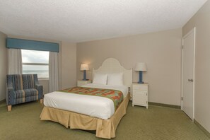 A hotel room with a bed, two bedside tables with lamps, a chair, a window with curtains, and a door.