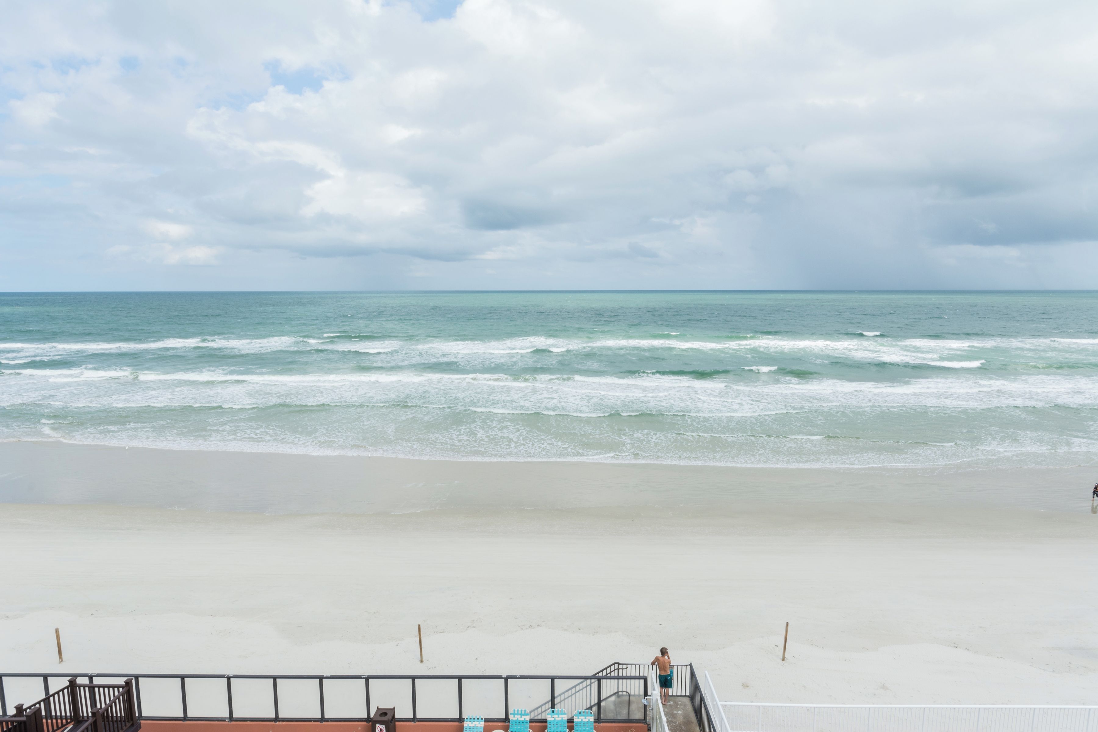 A beach view with a staircase leading down to the sand, a railing, and a person standing at the top.