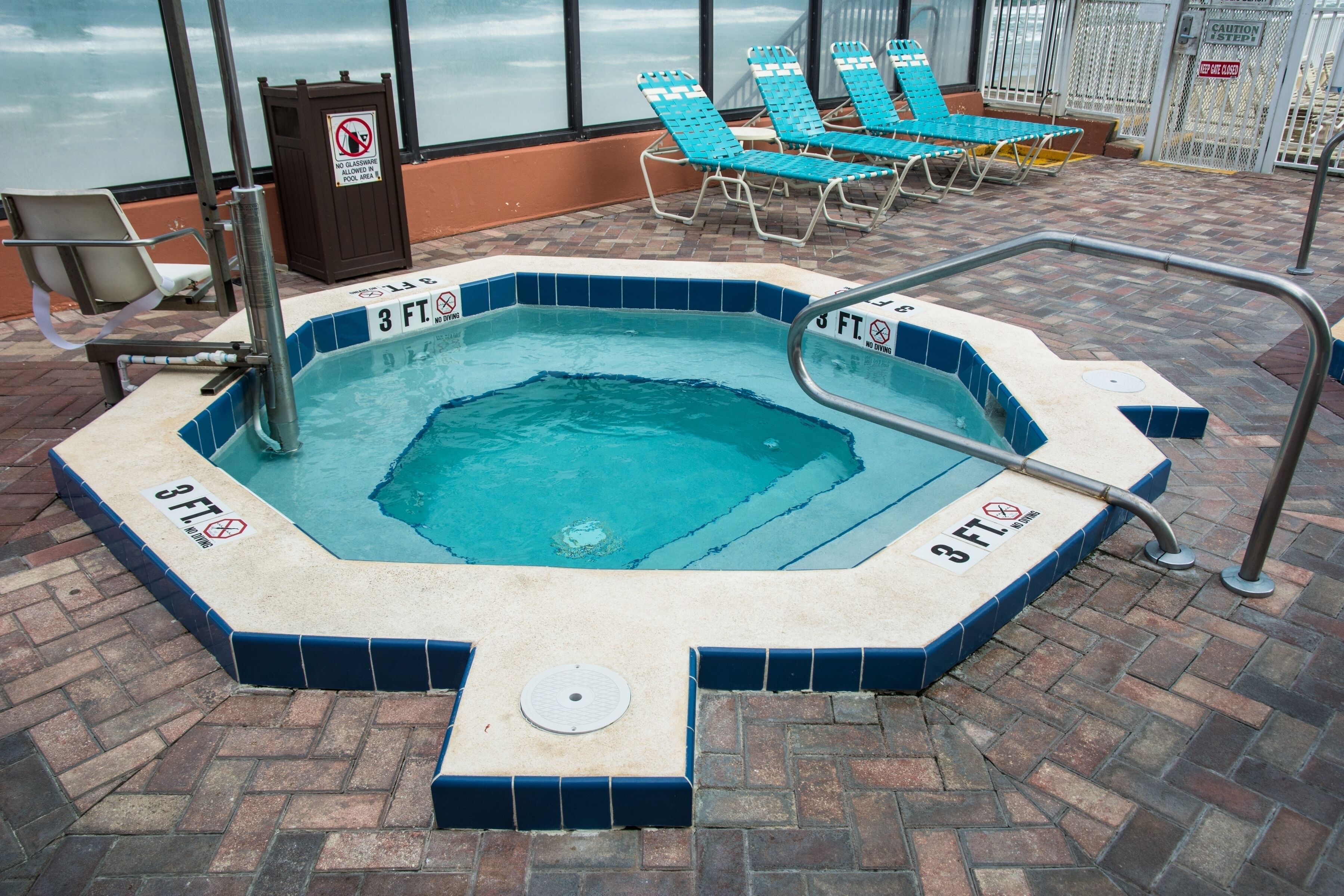 A hot tub with a 3 ft. no diving sign, surrounded by lounge chairs and a pool area.