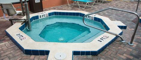 A hot tub with a 3 ft. no diving sign, surrounded by lounge chairs and a pool area.