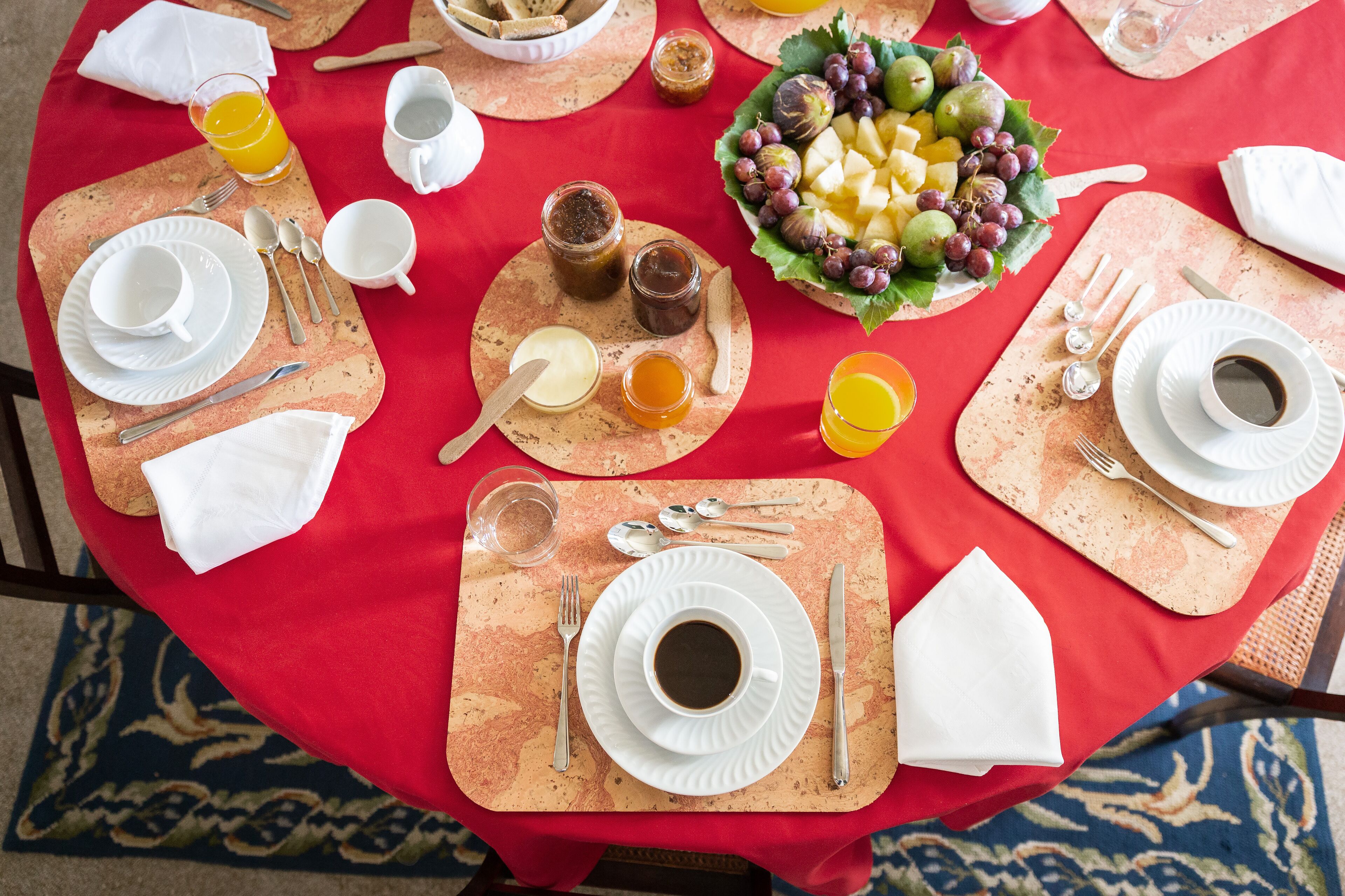 A table set for breakfast with plates, cups, cutlery, and a bowl of fruit.
