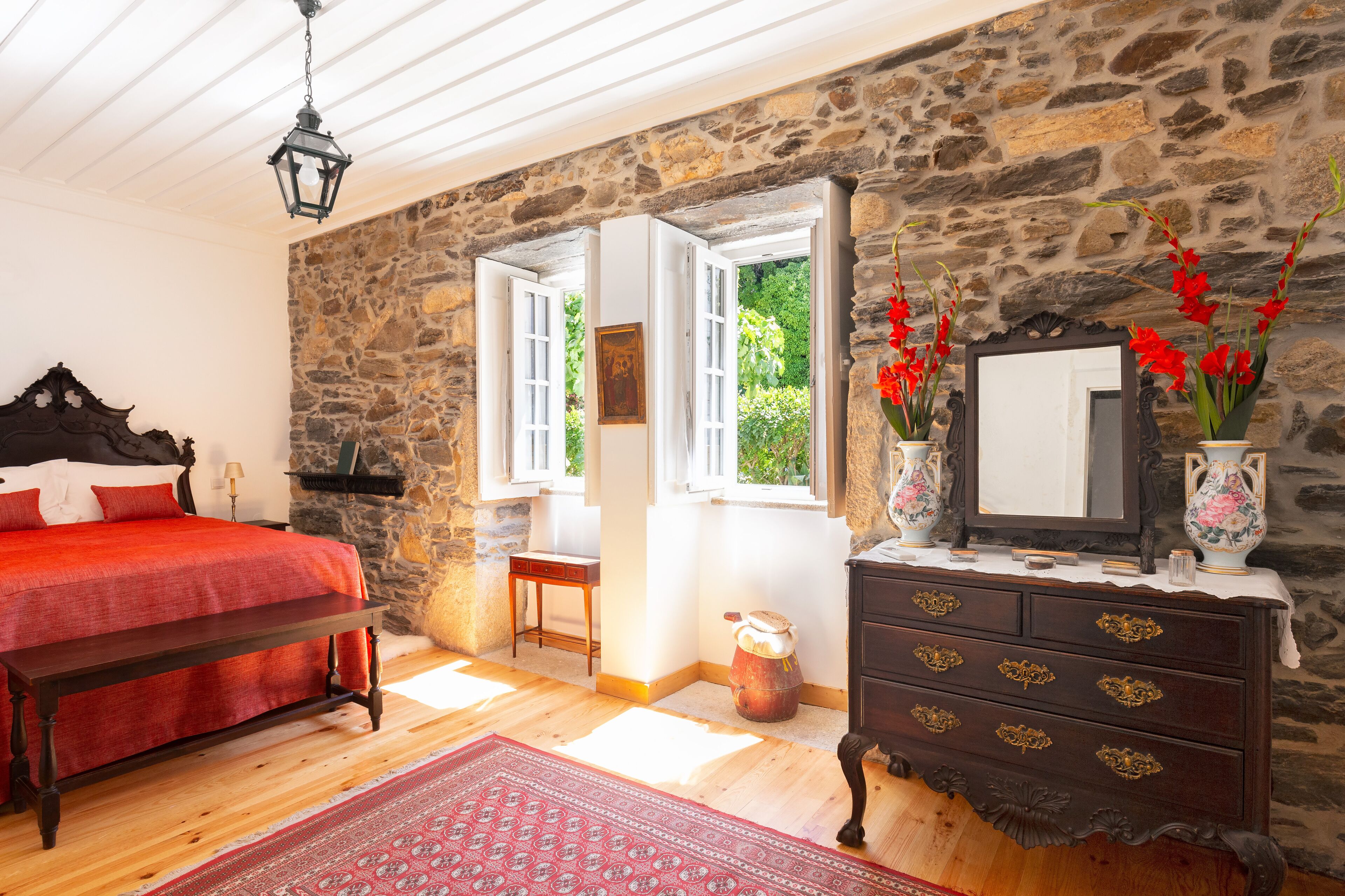 Une chambre avec un mur en pierre, un lit en bois, une commode et un miroir.