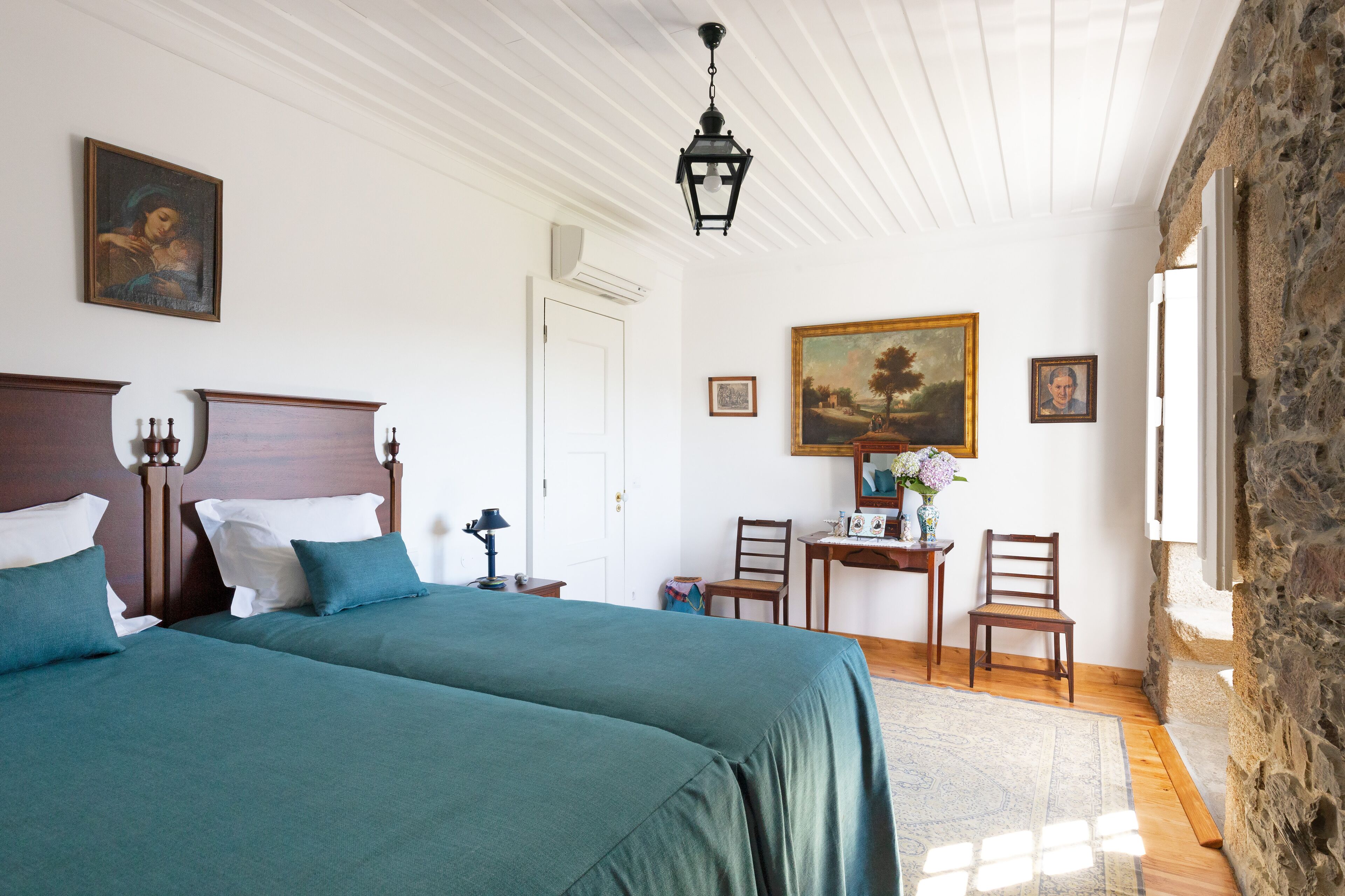 Quarto com duas camas, uma escrivaninha, cadeiras e um quadro na parede.