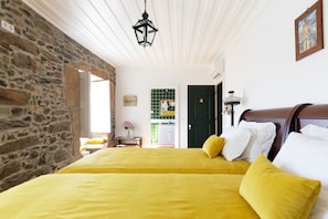 A bedroom with a stone wall, a bed with yellow bedding, a green door, and a hanging lantern. - Quinta do Valdalágea (Lamego)