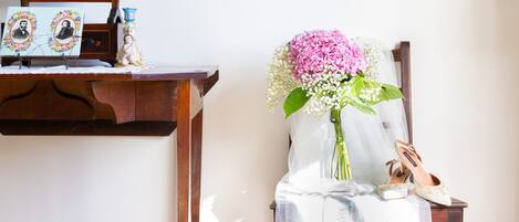 Ein hölzerner Stuhl mit weißem Stoff, eine Vase mit rosa Blumen und ein Paar Schuhe auf einem Tisch.