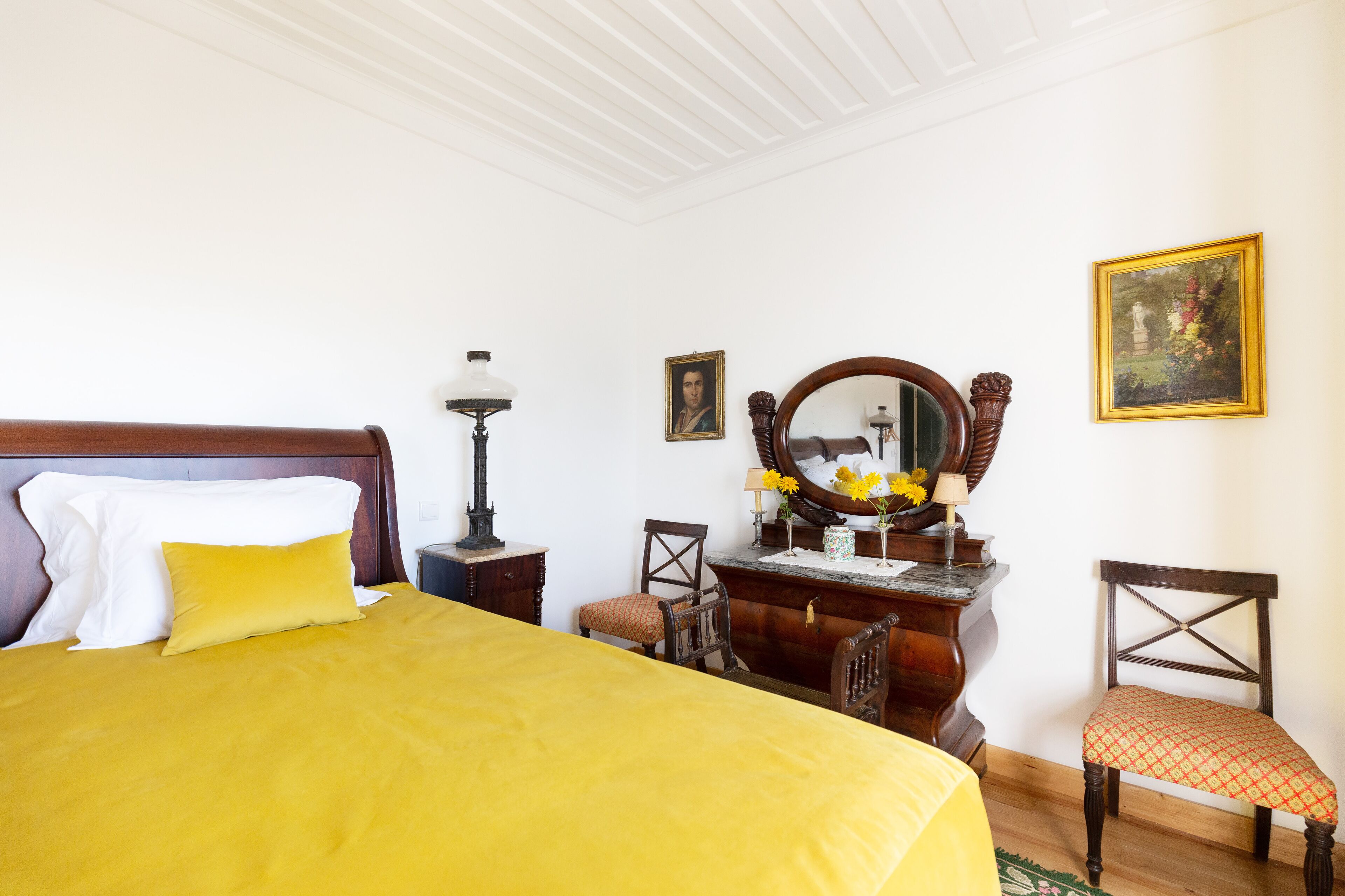 A neatly arranged bedroom with a large bed, a wooden dresser, a mirror, and a chair.