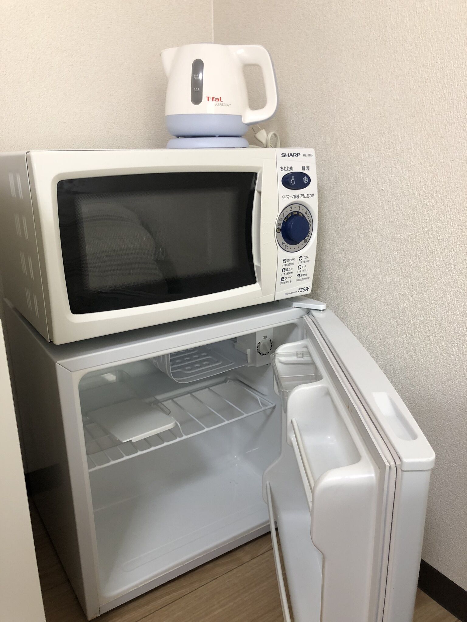 A microwave oven with a digital display and control panel, placed on top of a white refrigerator.