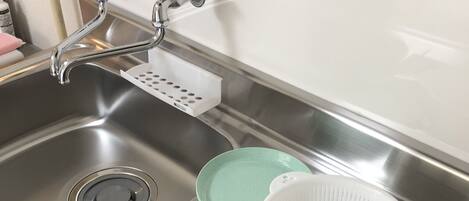A stainless steel kitchen sink with a black cutting board, a green plate, and a white colander.
