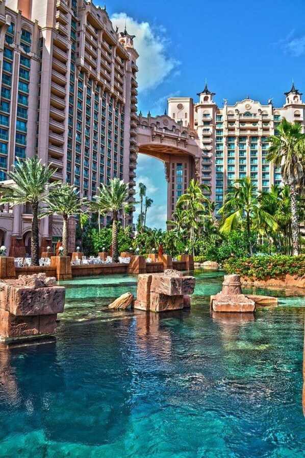 A resort with a large building, a water feature with rocks, and palm trees.