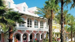 A pink and white building with arched windows and a covered patio area, surrounded by palm trees.