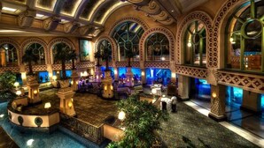 A luxurious lobby with ornate arches, a central fountain, and seating areas.