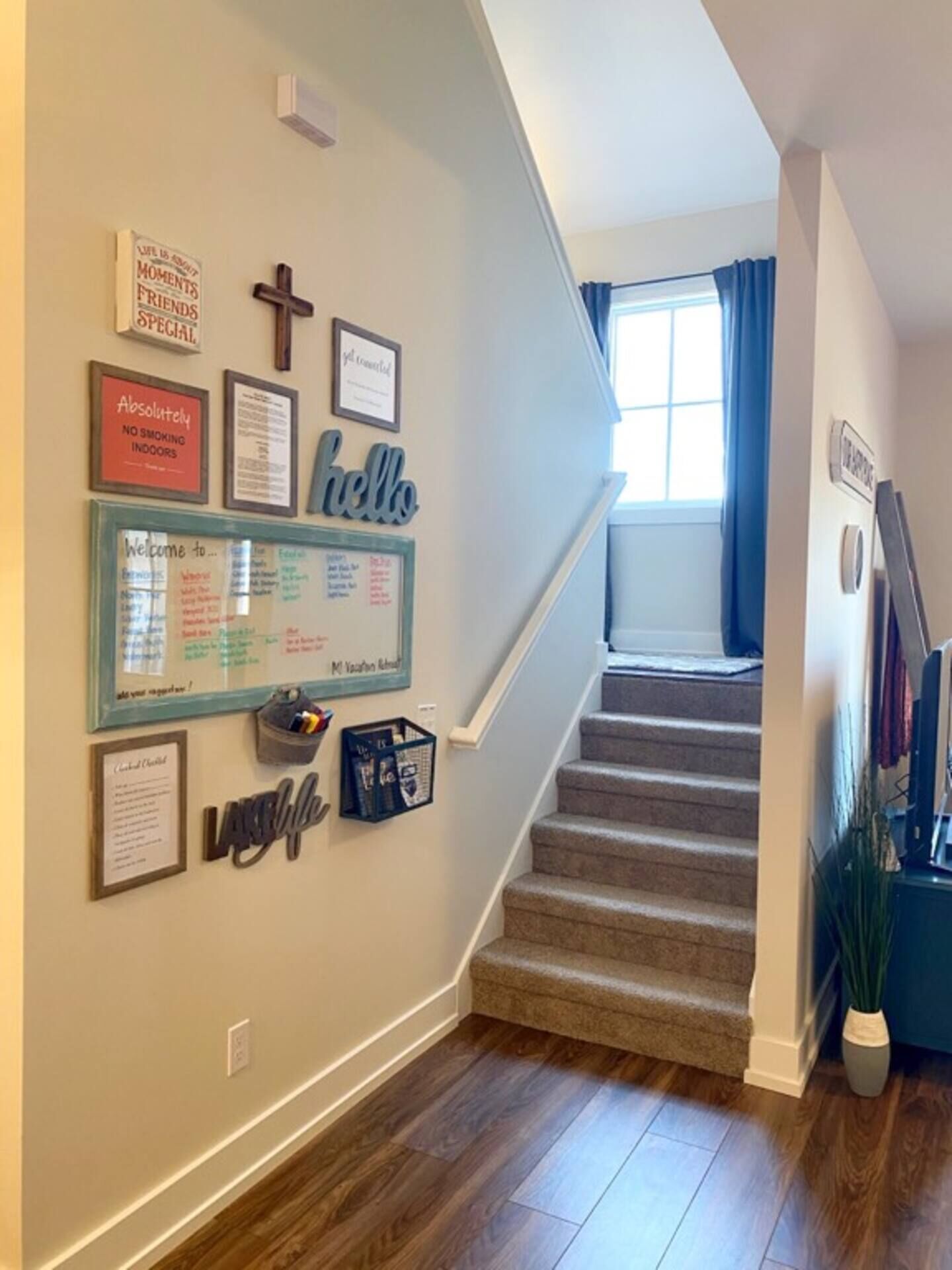 A staircase with a handrail, a wall with framed items, and a window with blue curtains.