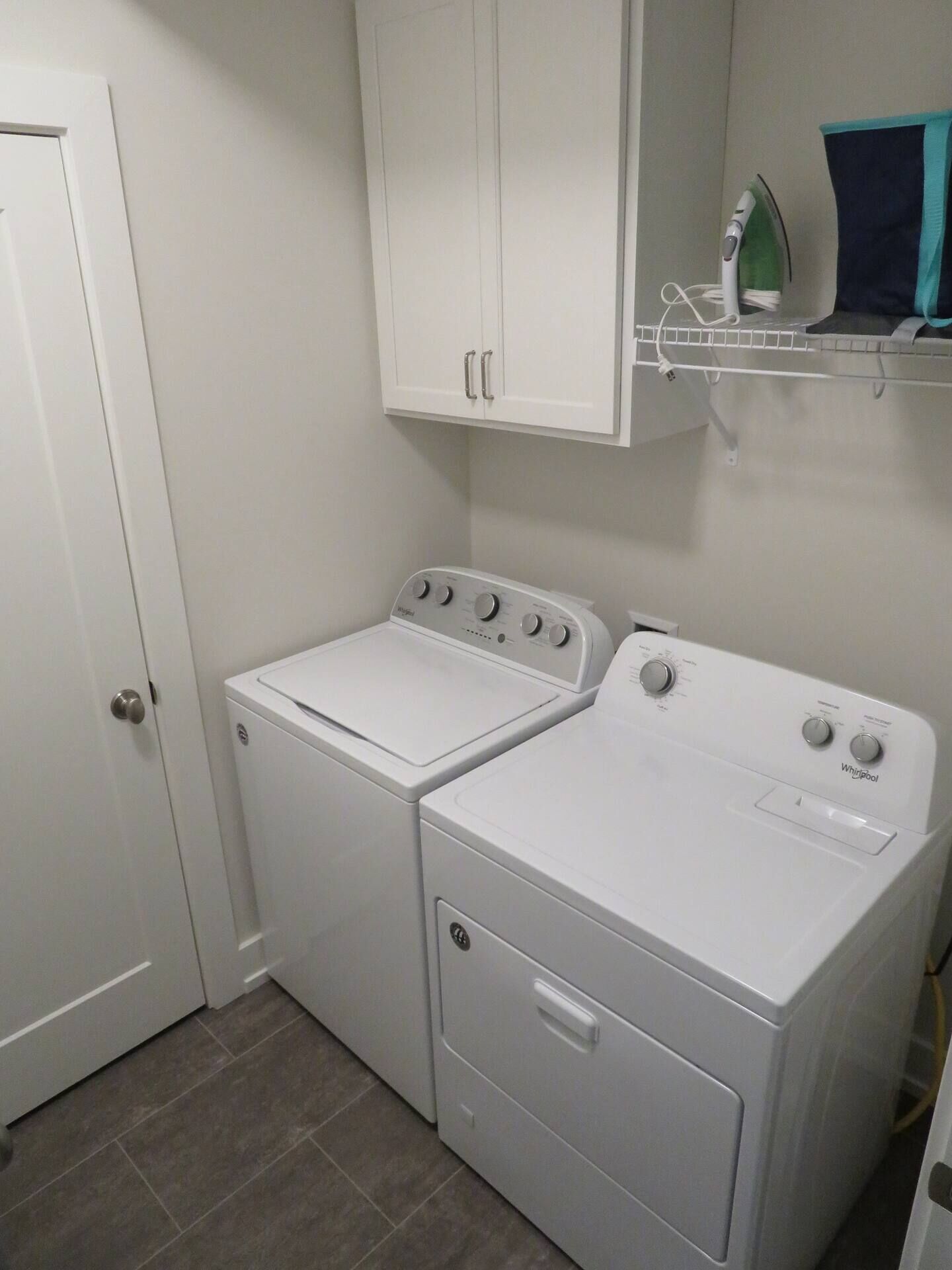 A laundry room with two white front-loading washers and dryers, a white door, and a white cabinet above the dryers.