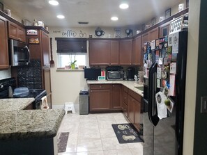 A kitchen with wooden cabinets, a microwave, a refrigerator, and a coffee-themed decor. - - Home Sweet Home - (Pembroke Pines)