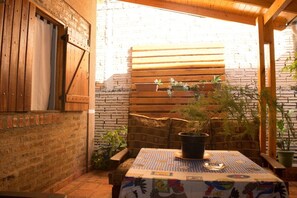 Un espacio al aire libre acogedor con mesa de madera, bancos acolchados y plantas en macetas.