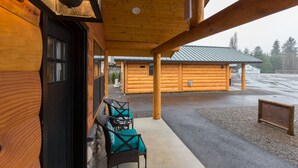 A log cabin with a covered porch, outdoor seating, and a gravel driveway.