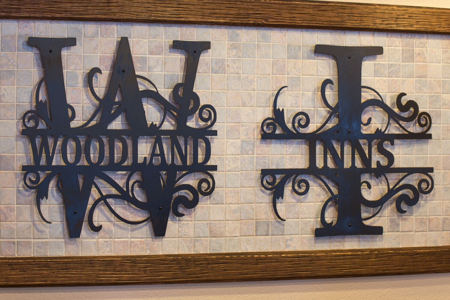 A decorative metal sign with the words "WAT WOODLAND" and "WAT INNS" on a tiled wall.