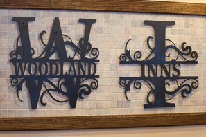 A decorative metal sign with the words "WAT WOODLAND" and "WAT INNS" on a tiled wall.