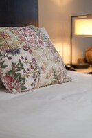 Una cama con un cojín estampado con motivos florales y una lámpara de noche.