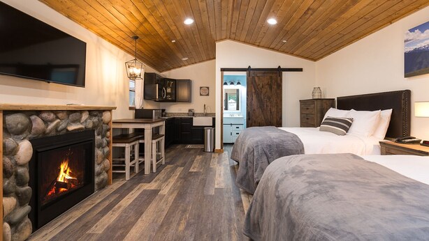 A cozy room with a fireplace, a kitchen area, and two beds.