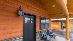 A log cabin with a black door, stone foundation, and a covered porch with wicker chairs.