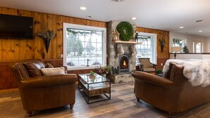 A cozy living room with a stone fireplace, leather sofas, and large windows. - Woodland Inns (Forks)